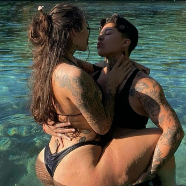 One person holding the other in their arms while they face each other, both of them are standing in the water